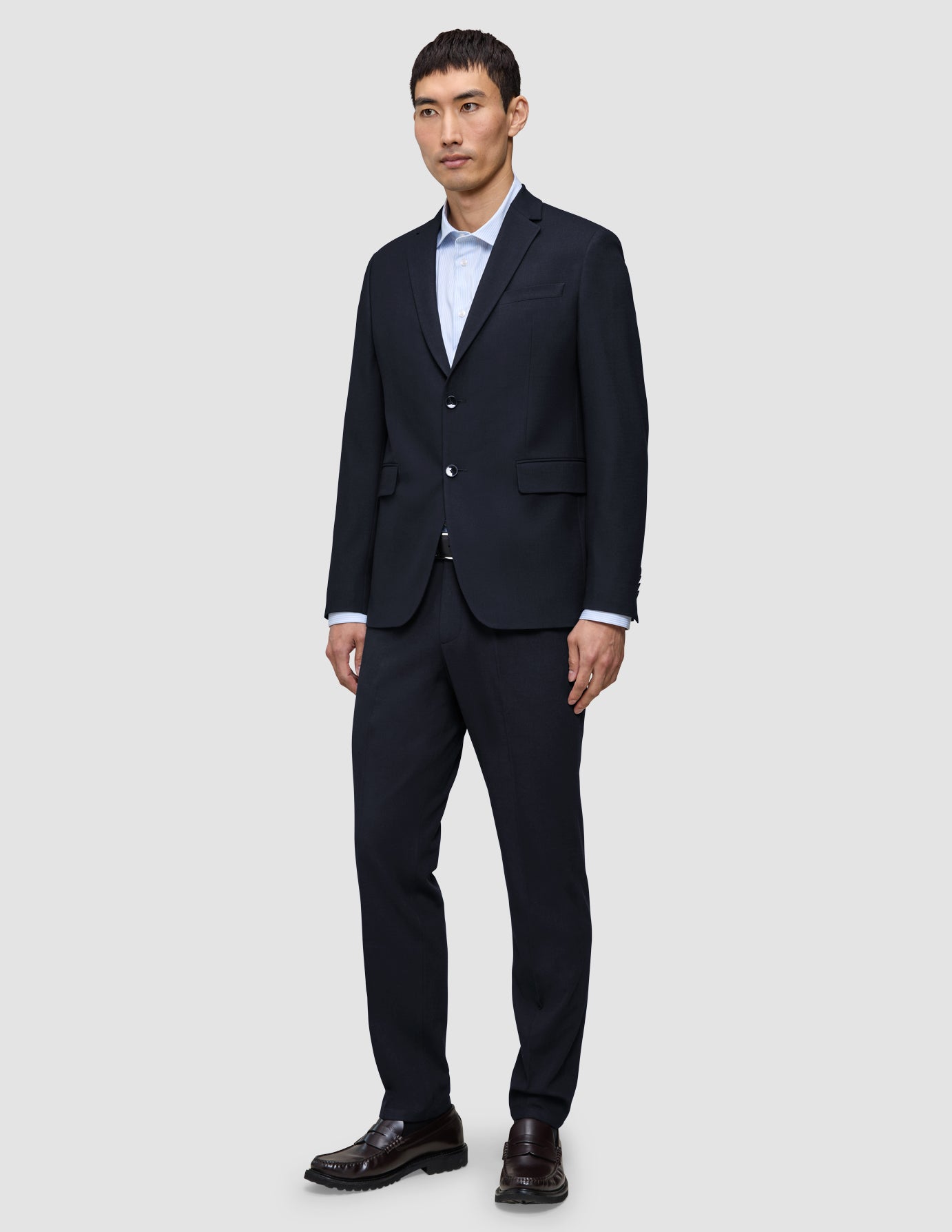 A man wears a Motion Blazer Slim Midnight Blue jacket and matching trousers, paired with a light blue button-down shirt and dark leather loafers.