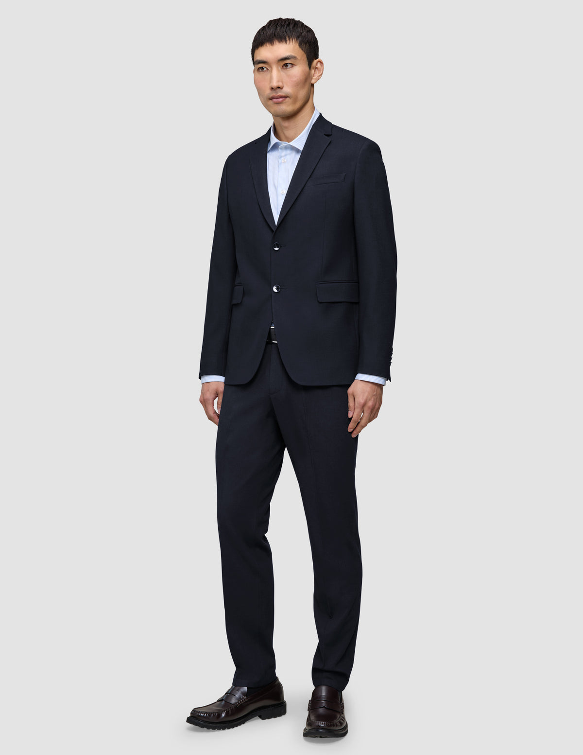 A man wears a Motion Blazer Slim Midnight Blue jacket and matching trousers, paired with a light blue button-down shirt and dark leather loafers.