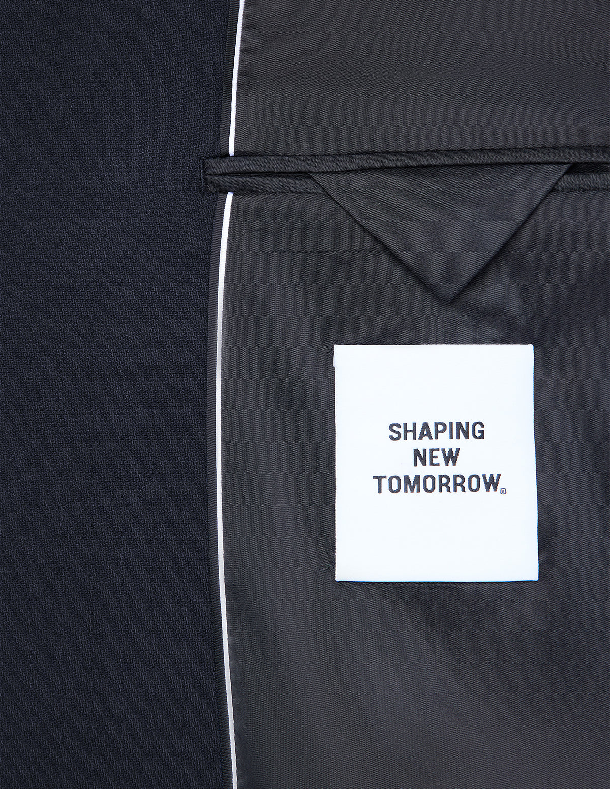Interior view of a dark blue Motion Blazer Slim Midnight Blue, showing a white SHAPING NEW TOMORROW label stitched to the black lining of the 360° stretch tailored blazer.