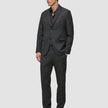A person wearing a Motion Blazer Slim Pepper Grey with matching trousers over a dark brown button-up shirt and dark loafers, crafted from lightweight breathable fabric.