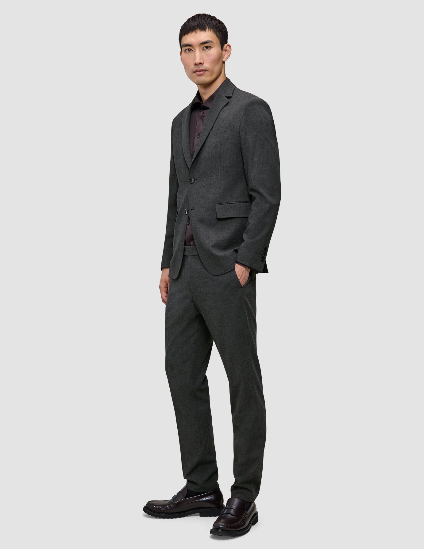 A man wearing a Motion Blazer Slim Pepper Grey over a dark button-down shirt, standing with one hand in his pocket.
