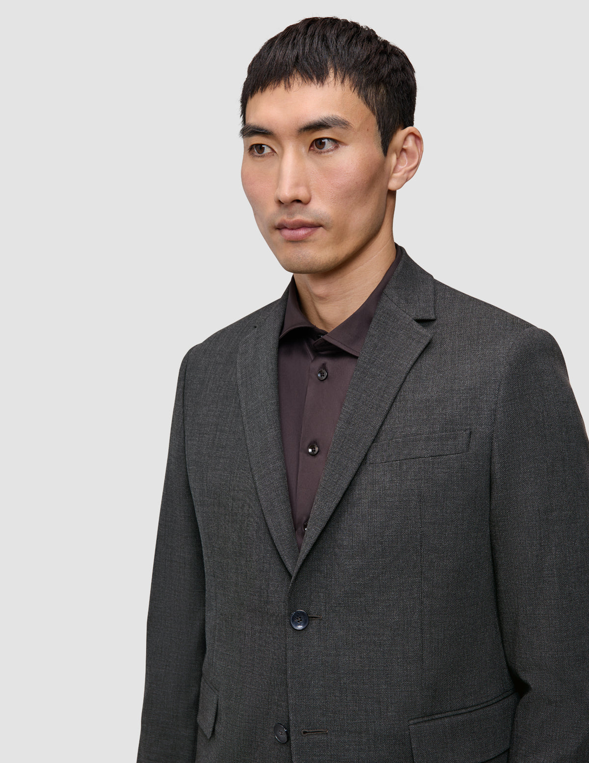 A man wears a Motion Blazer Slim Pepper Grey in a tailored, 360° stretch grey fabric over a dark brown button-up shirt.