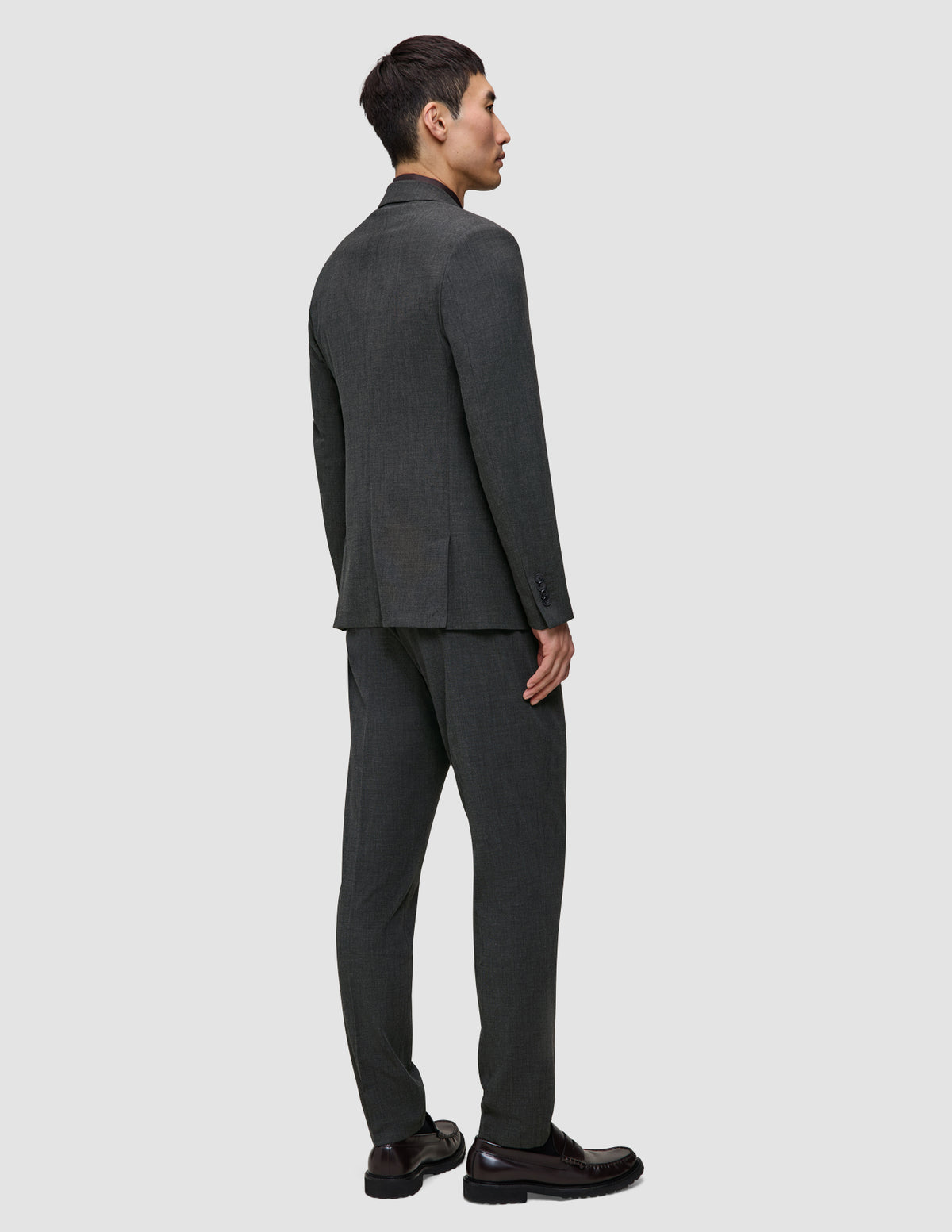 A man seen from behind wearing a Motion Blazer Slim Pepper Grey and matching trousers with dark loafers.