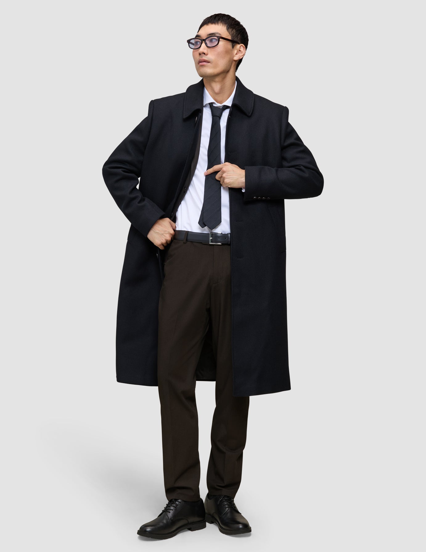 A man wearing a black overcoat, white dress shirt, dark tie, and Motion Suit Pants Regular Cognac.