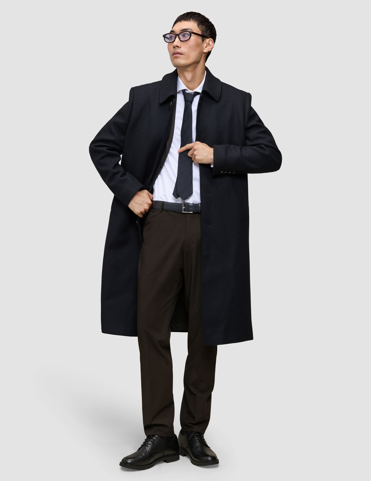 A man wearing a black overcoat, white dress shirt, dark tie, and Motion Suit Pants Regular Cognac.