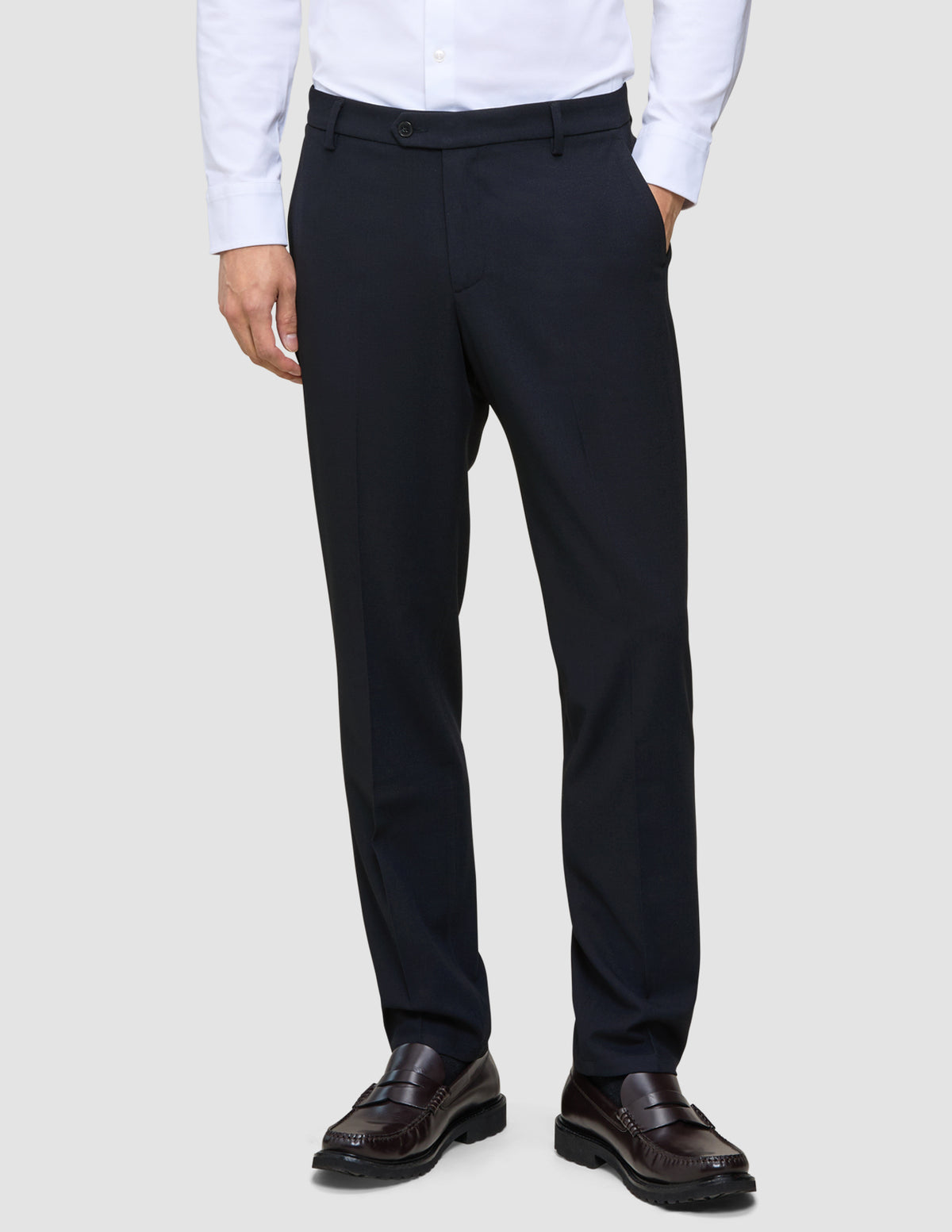 A man wearing a white dress shirt, Motion Suit Pants Regular Midnight Blue, and dark brown loafers.