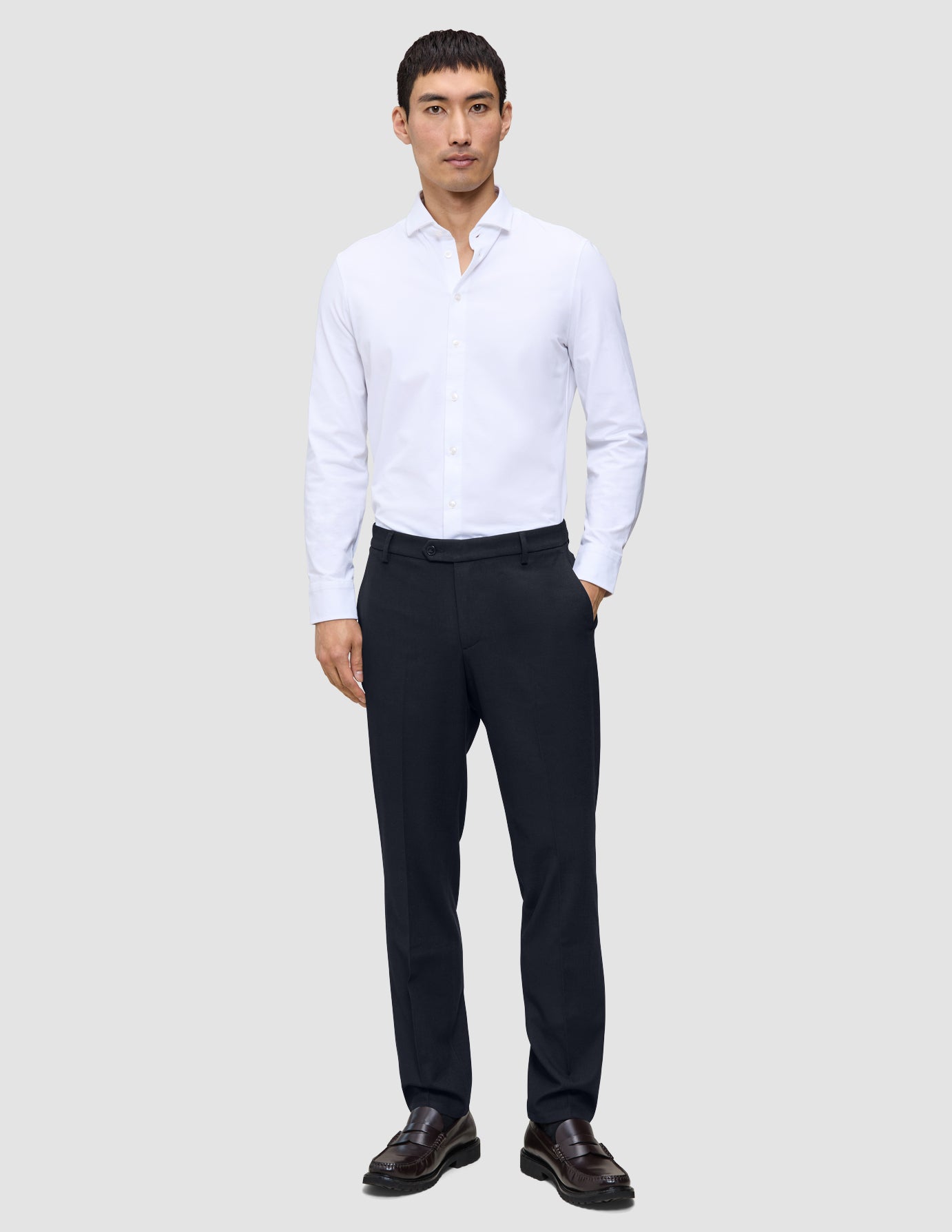 A man wearing a white button-down shirt, Motion Suit Pants Regular Midnight Blue, and dark leather loafers.