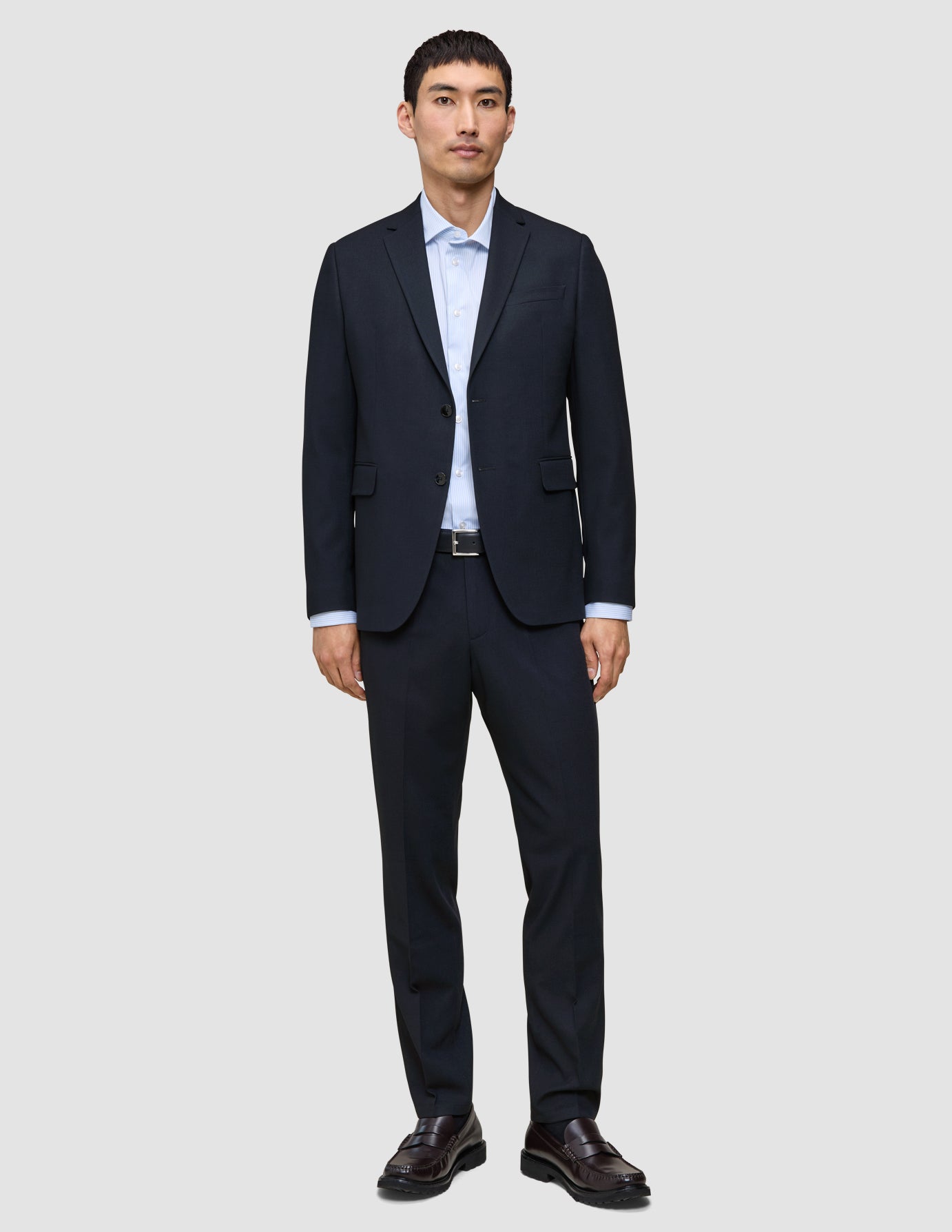 A man wearing Motion Suit Pants Regular Midnight Blue with a matching lightweight navy suit jacket, a light blue button-down shirt, and dark leather loafers.