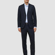 A man wearing Motion Suit Pants Regular Midnight Blue with a matching lightweight navy suit jacket, a light blue button-down shirt, and dark leather loafers.