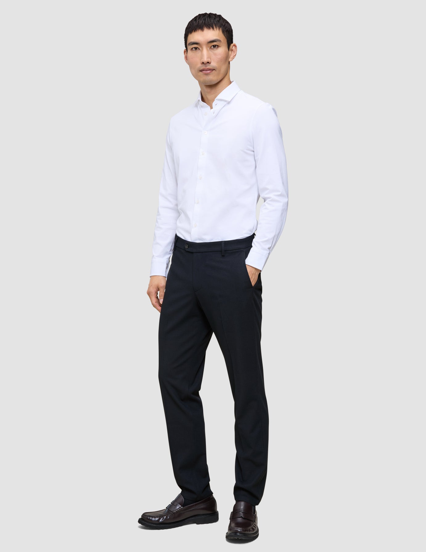 A man in a white button-down shirt and Motion Suit Pants Regular Midnight Blue stands with his hand in his pocket.