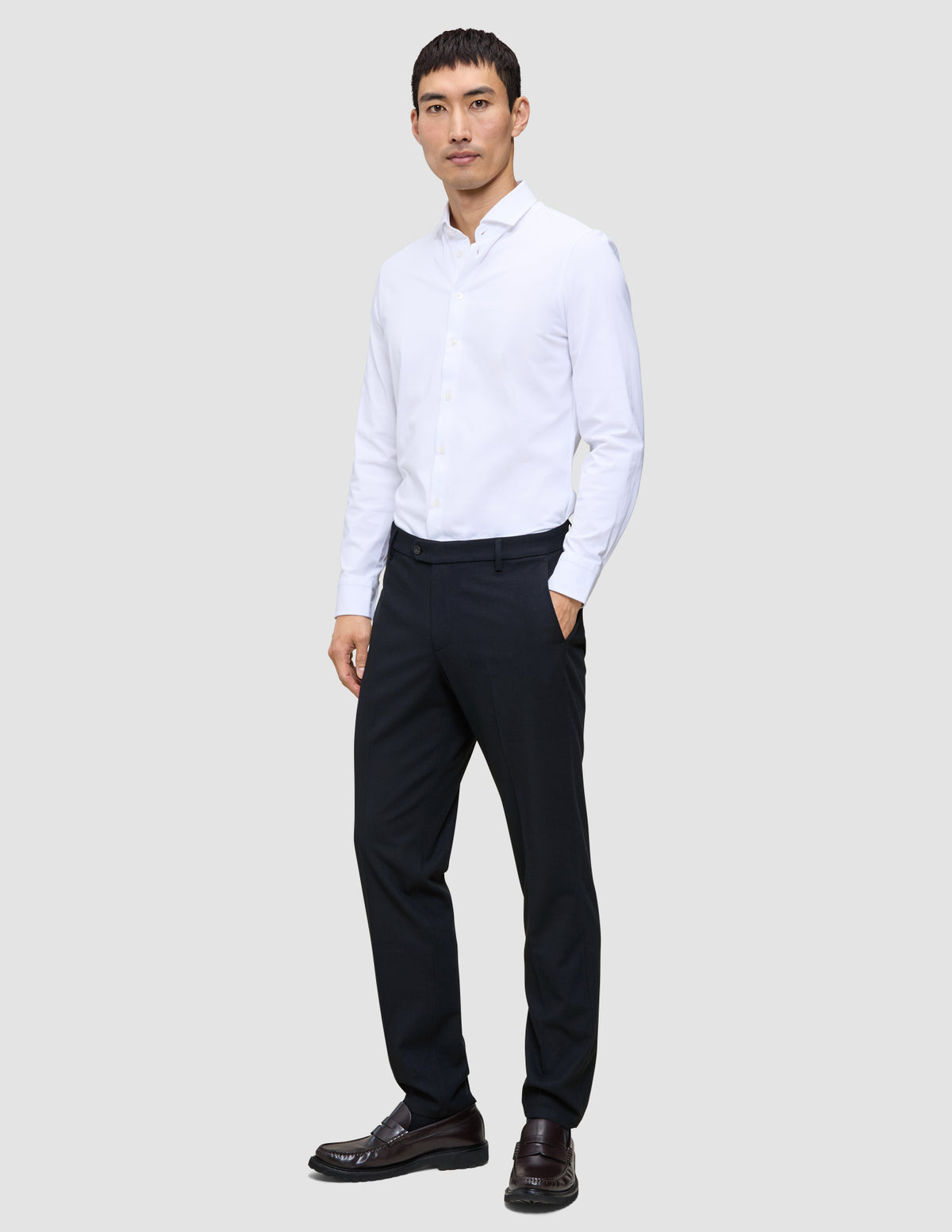 A man in a white button-down shirt and Motion Suit Pants Regular Midnight Blue stands with his hand in his pocket.