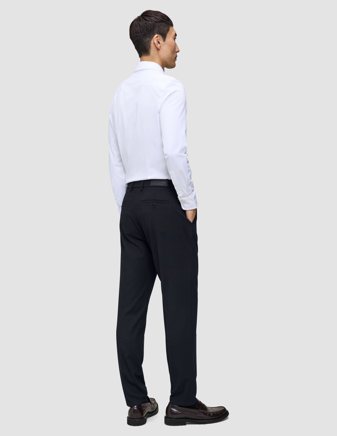 A man viewed from behind, wearing a white button-down shirt and Motion Suit Pants Regular Midnight Blue with his hands in his pockets.