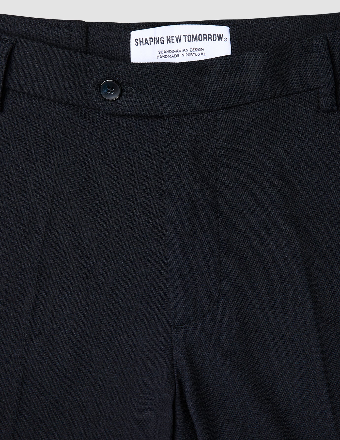 Close-up of the waistband and top of Motion Suit Pants Regular Midnight Blue, featuring a button closure and internal brand label on 360° stretch dark blue fabric.