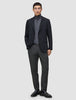 A man wears a black blazer, a grey turtleneck, and Motion Suit Pants Regular Pepper Grey, paired with a black leather belt and black loafers.