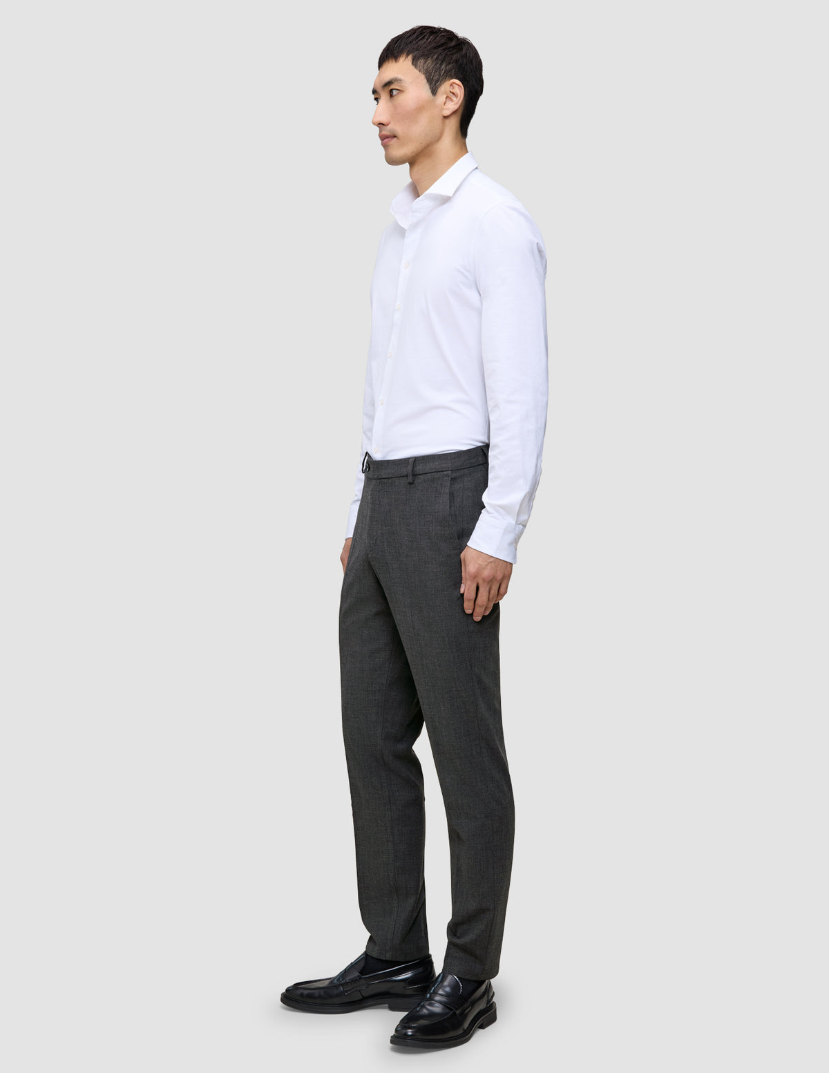 A person seen from the side wearing a white button-down shirt, Motion Suit Pants Regular Pepper Grey, and black loafers.