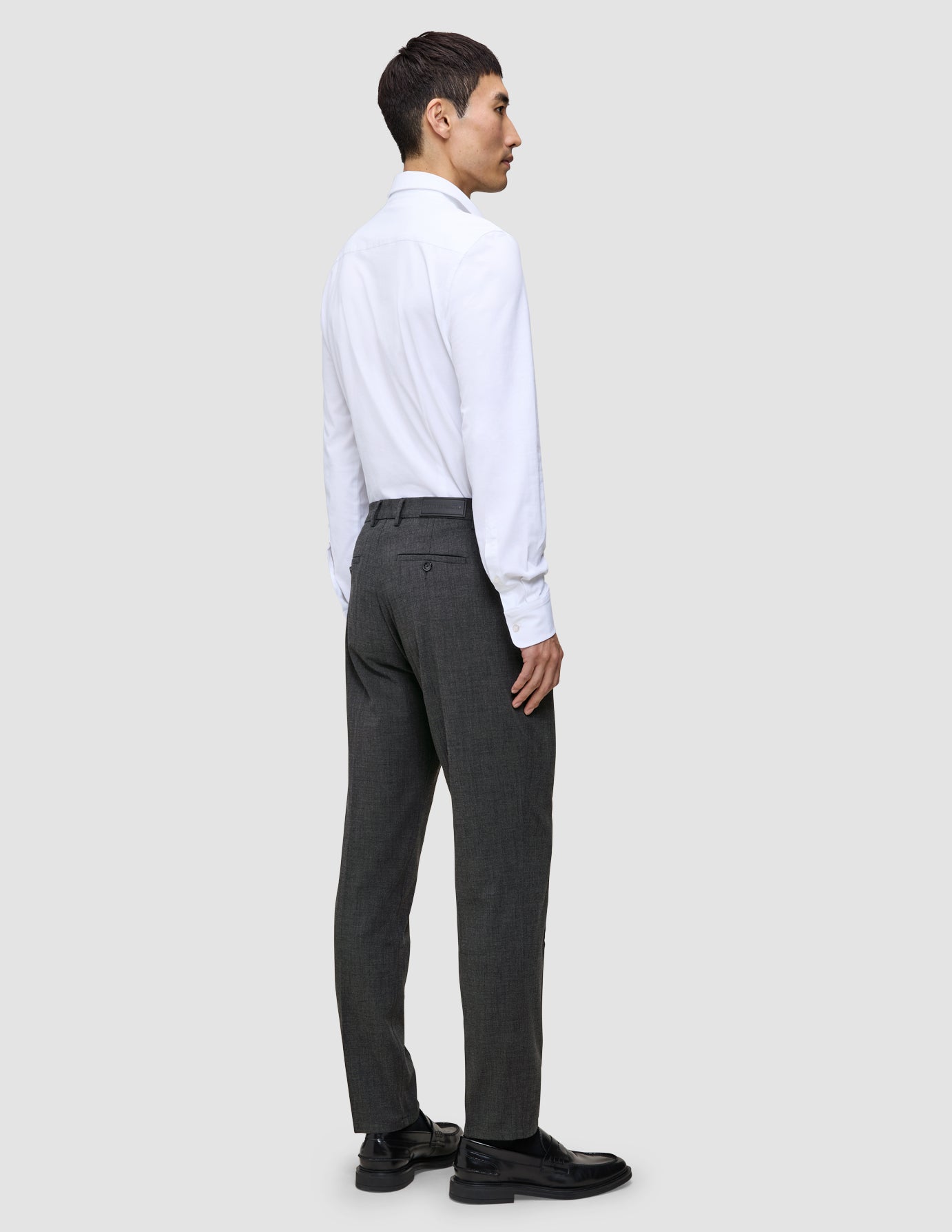 A person seen from behind wears a white button-down shirt, Motion Suit Pants Regular Pepper Grey, and black loafers.
