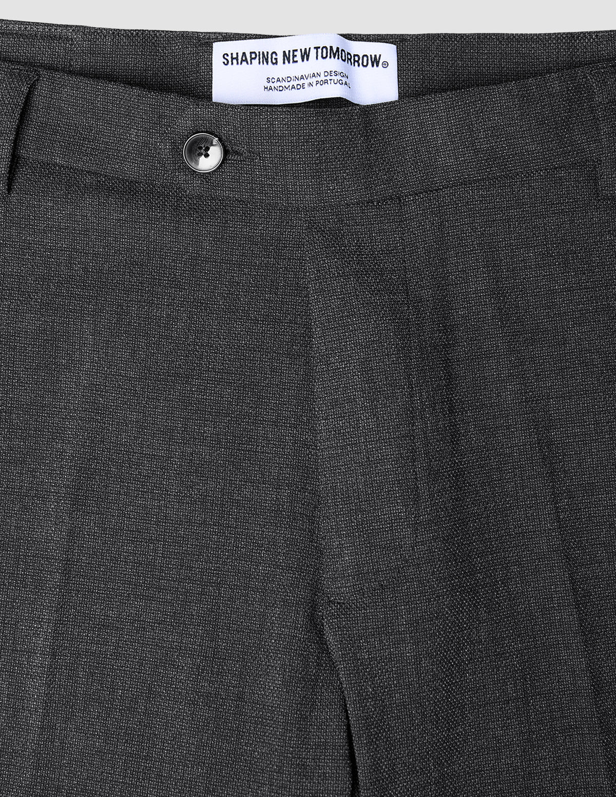 Close-up of Motion Suit Pants Regular Pepper Grey in charcoal grey 360° stretch fabric, featuring a button closure and a brand label at the waistband.