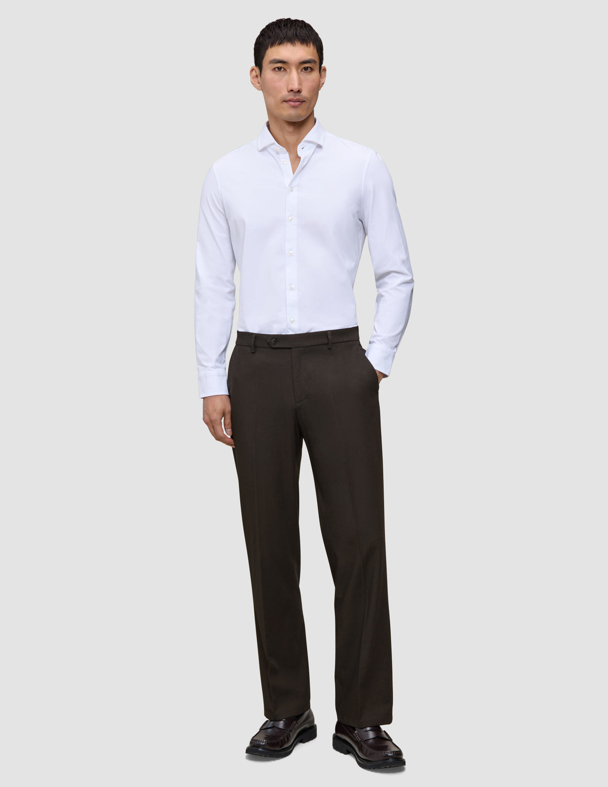 A man wears a white button-down shirt with a relaxed fit, Motion Suit Pants Relaxed Cognac, and dark loafers.
