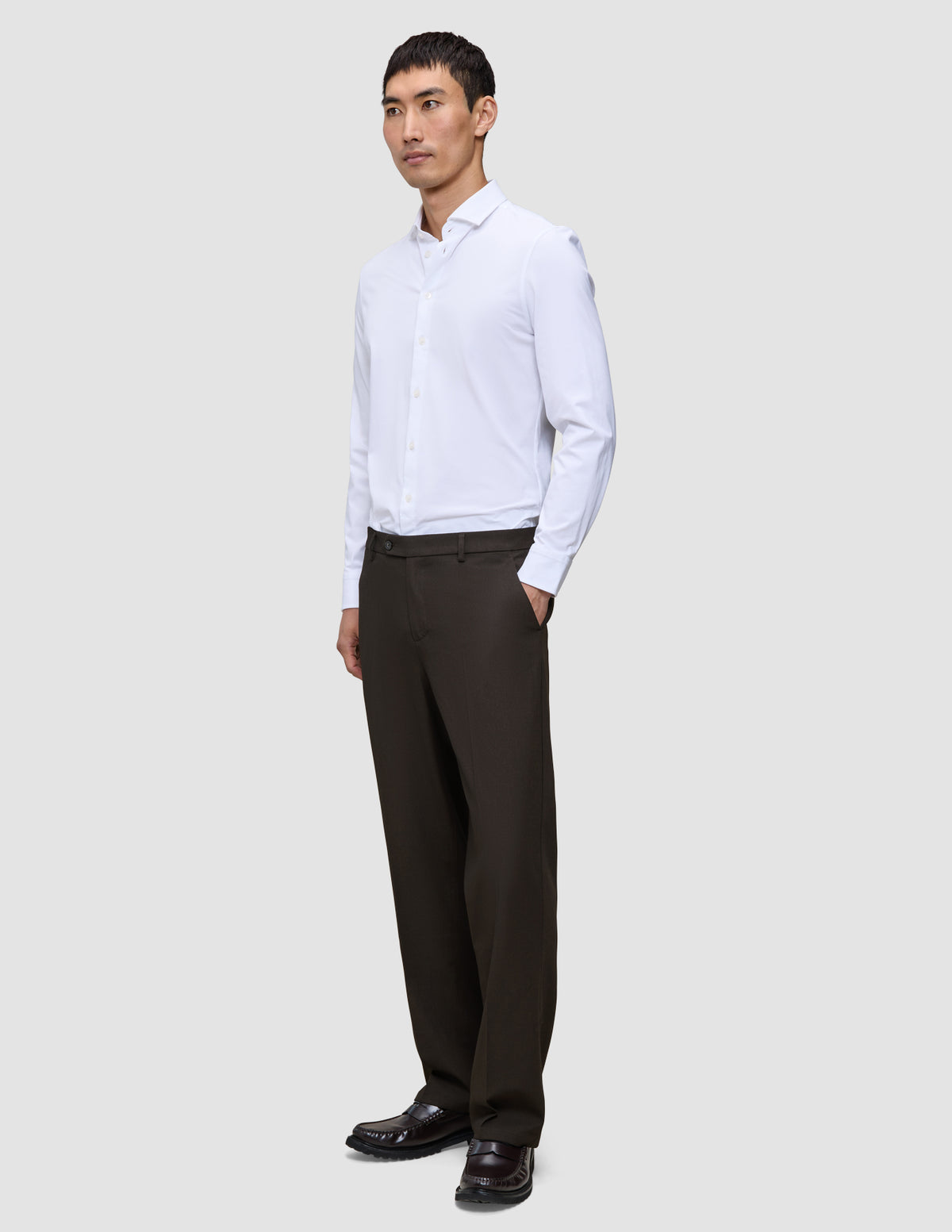 A man wearing a white button-down shirt, dark loafers, and Motion Suit Pants Relaxed Cognac.
