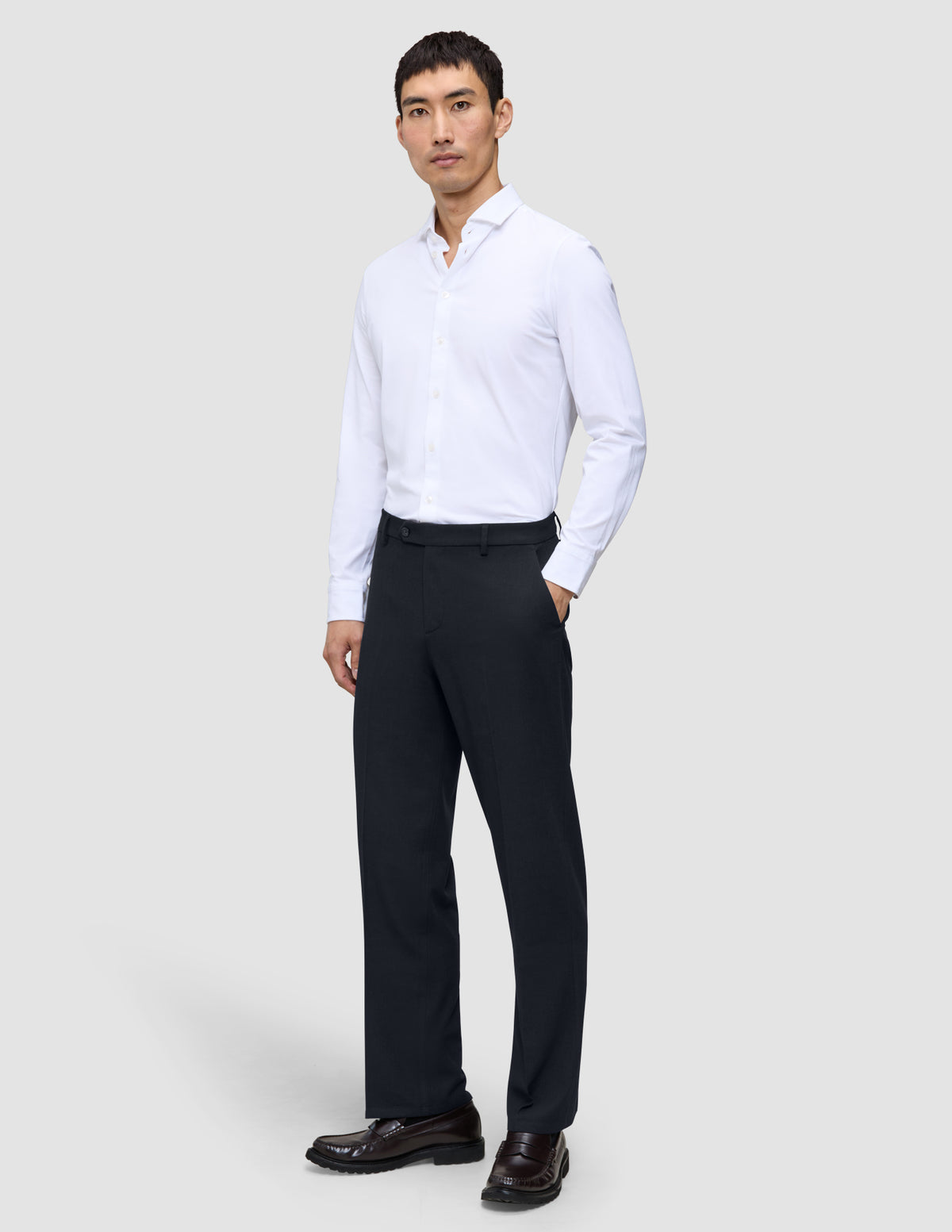 A man wearing a white button-down shirt and Motion Suit Pants Relaxed Midnight Blue, paired with dark brown loafers.