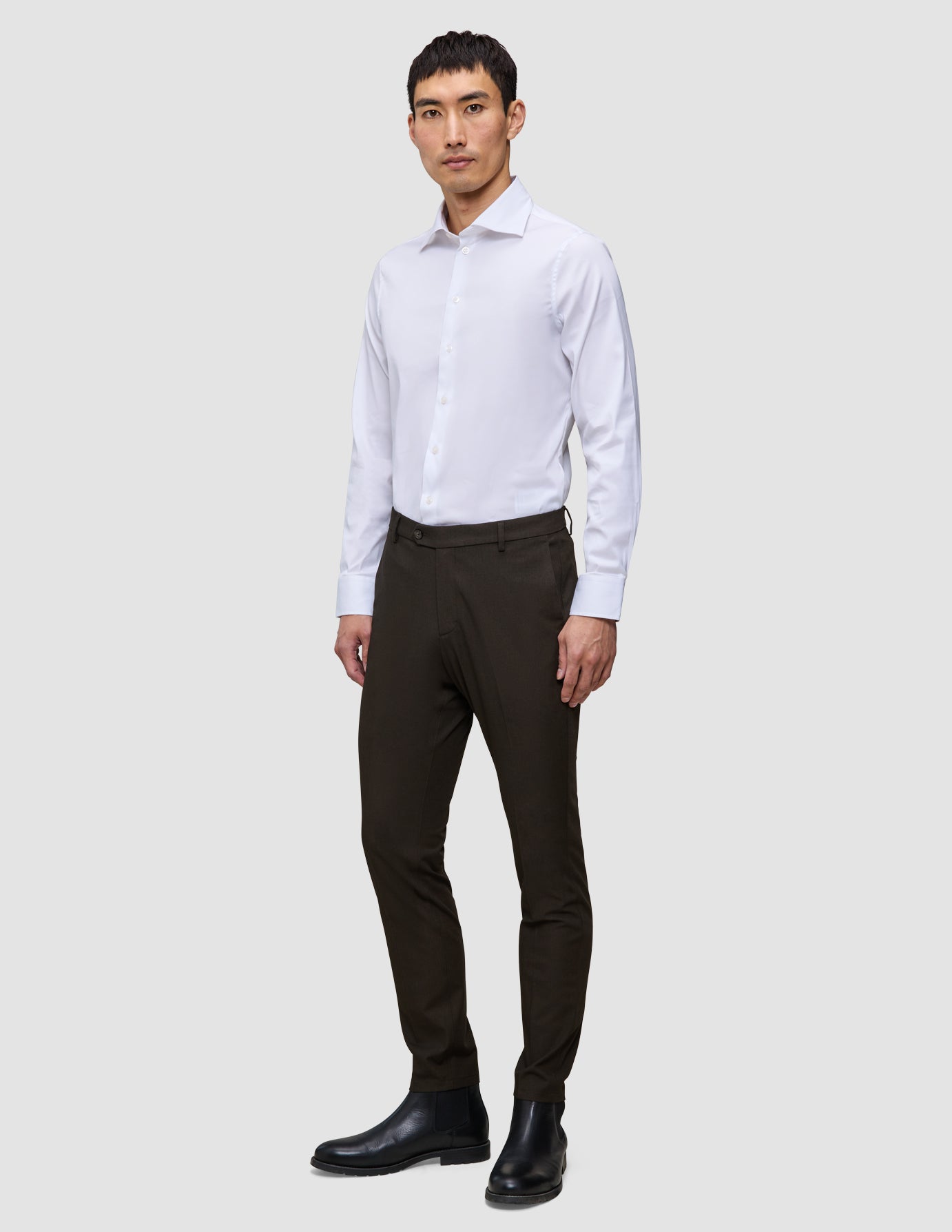 A man wearing a white dress shirt, Motion Suit Pants Slim Cognac, and black leather boots.