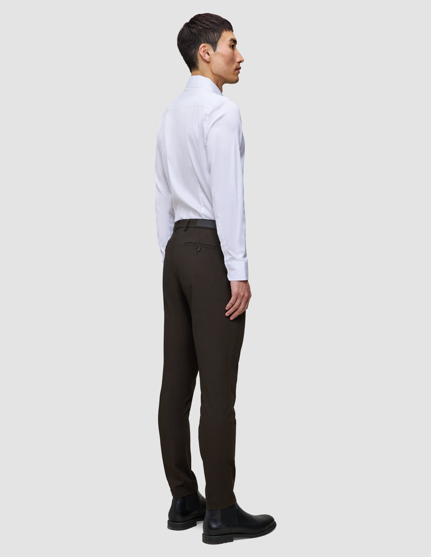 A man in profile wears a white dress shirt, slim-fit Motion Suit Pants Slim Cognac, and black leather boots.