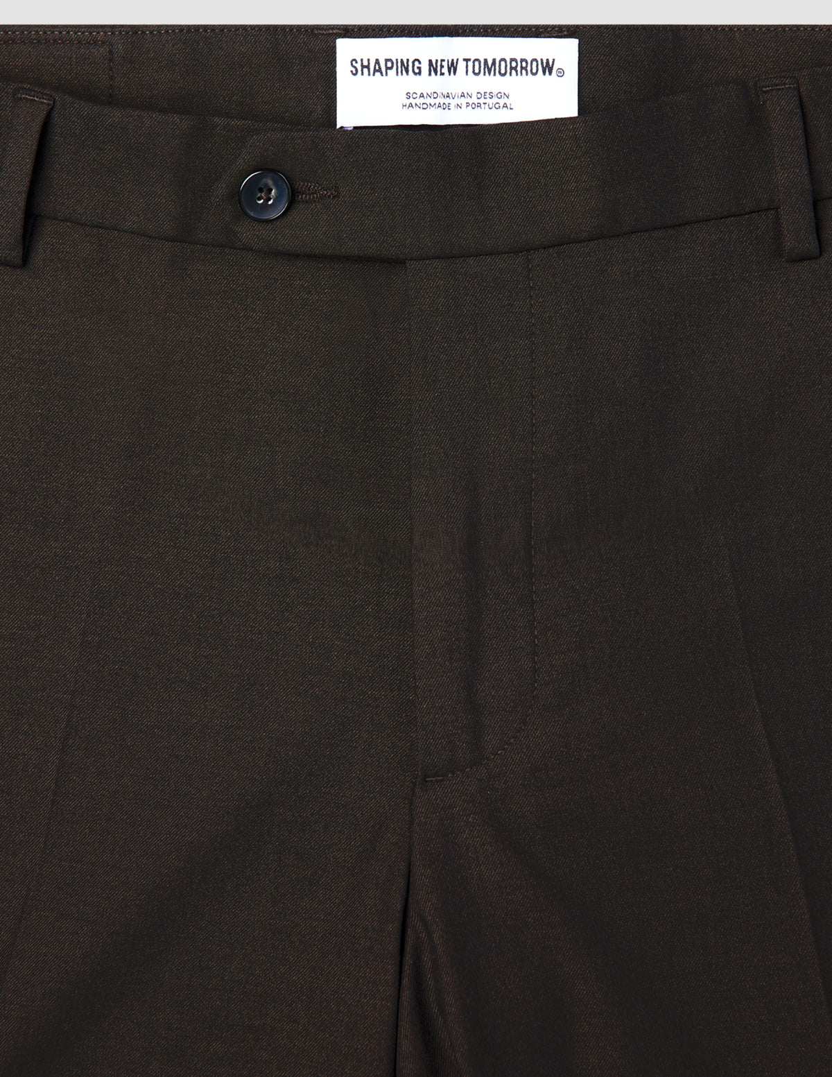 Close-up of Motion Suit Pants Slim Cognac in lightweight, breathable brown fabric, featuring a dark button and a brand label at the waistband.