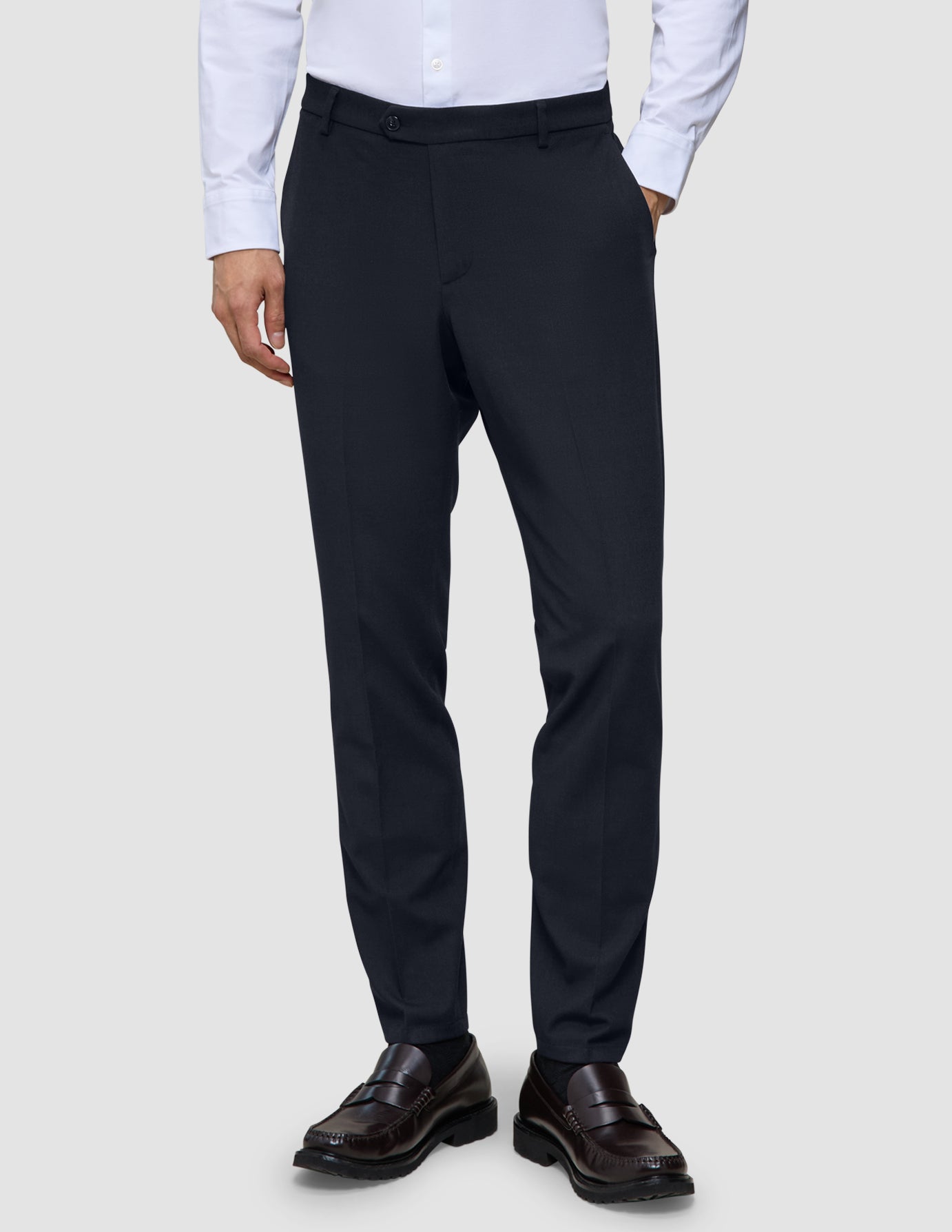 A person wearing a white button-down shirt, Motion Suit Pants Slim Midnight Blue, and dark leather loafers.