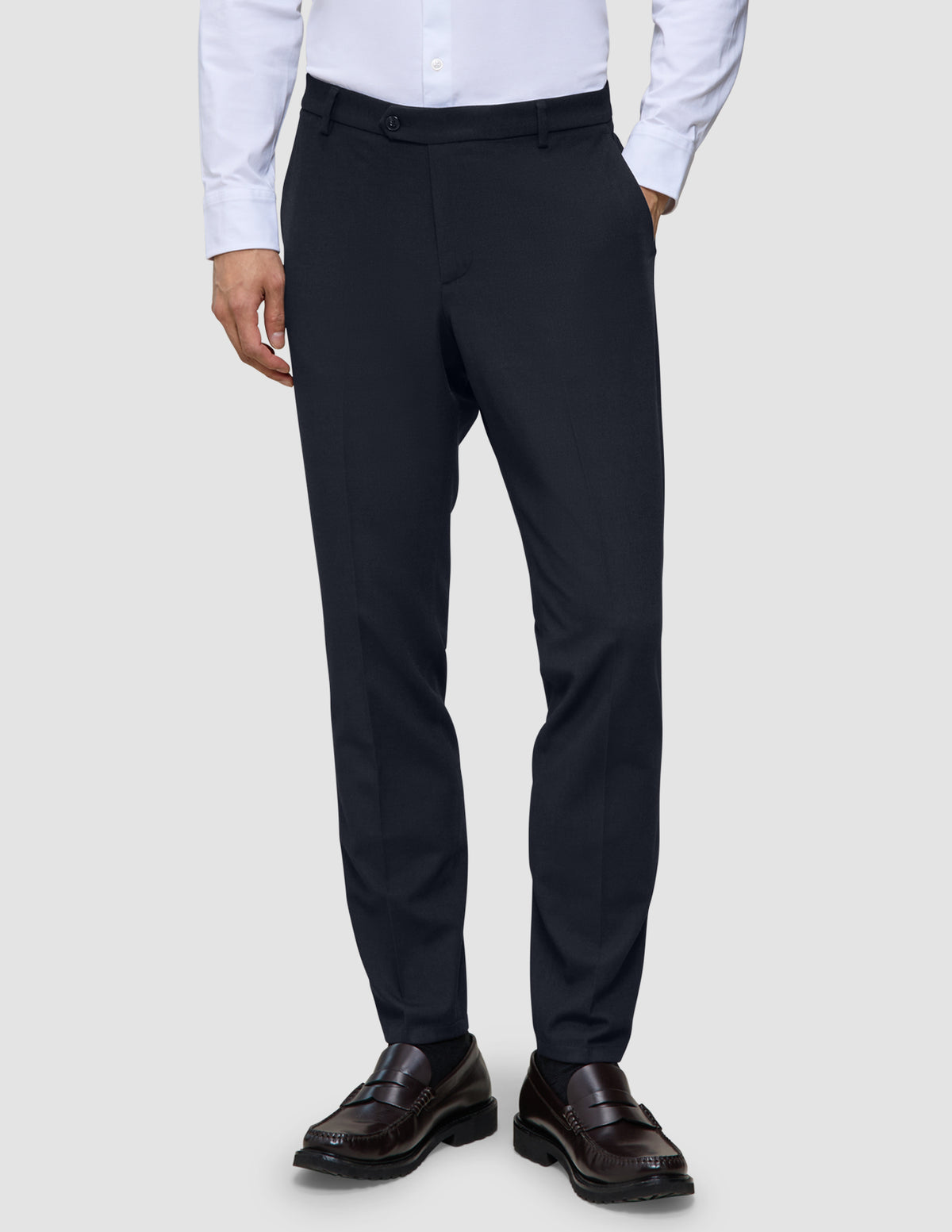 A person wearing a white button-down shirt, Motion Suit Pants Slim Midnight Blue, and dark leather loafers.