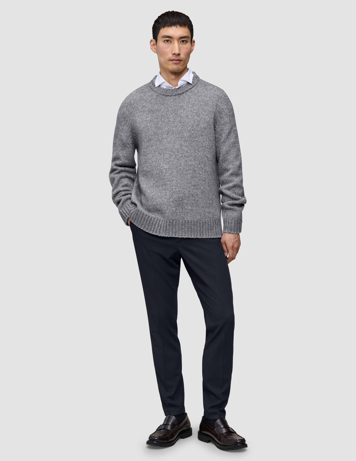 A man wearing a grey crew-neck sweater over a white collared shirt, paired with Motion Suit Pants Slim Midnight Blue and dark brown loafers.