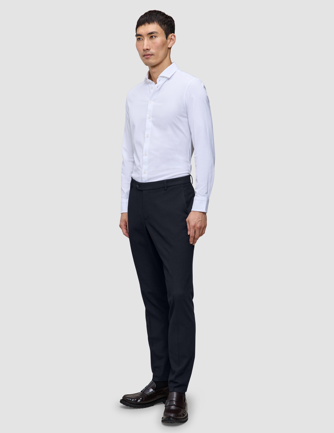 A man stands wearing a white button-down shirt and Midnight Blue Motion Suit Pants Slim made of breathable fabric.
