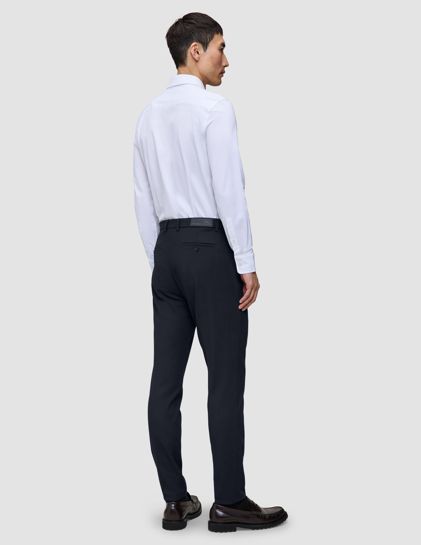 A man seen from behind wearing a white button-down shirt, Motion Suit Pants Slim Midnight Blue, and dark loafers.