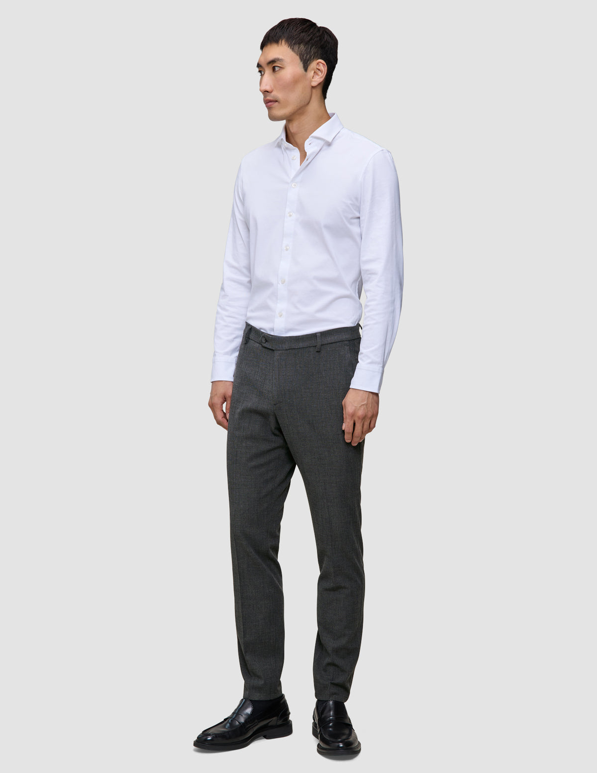A man wearing a white button-down shirt, Motion Suit Pants Slim Pepper Grey, and black dress shoes.
