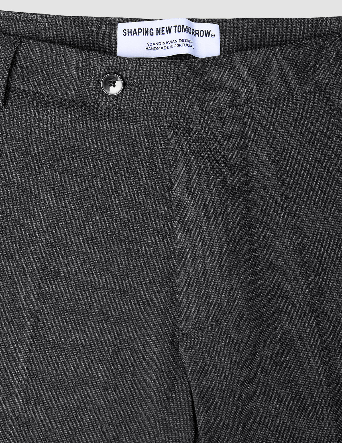 Close-up of the waistband and top of dark grey Motion Suit Pants Slim Pepper Grey, featuring a single button closure, 360° stretch slim-fit, and an interior brand label reading Shaping New Tomorrow.