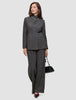 A person wearing The suit with a statement, featuring a classic check high-neck Nara Blazer and wide-leg trousers, carrying a black handbag.