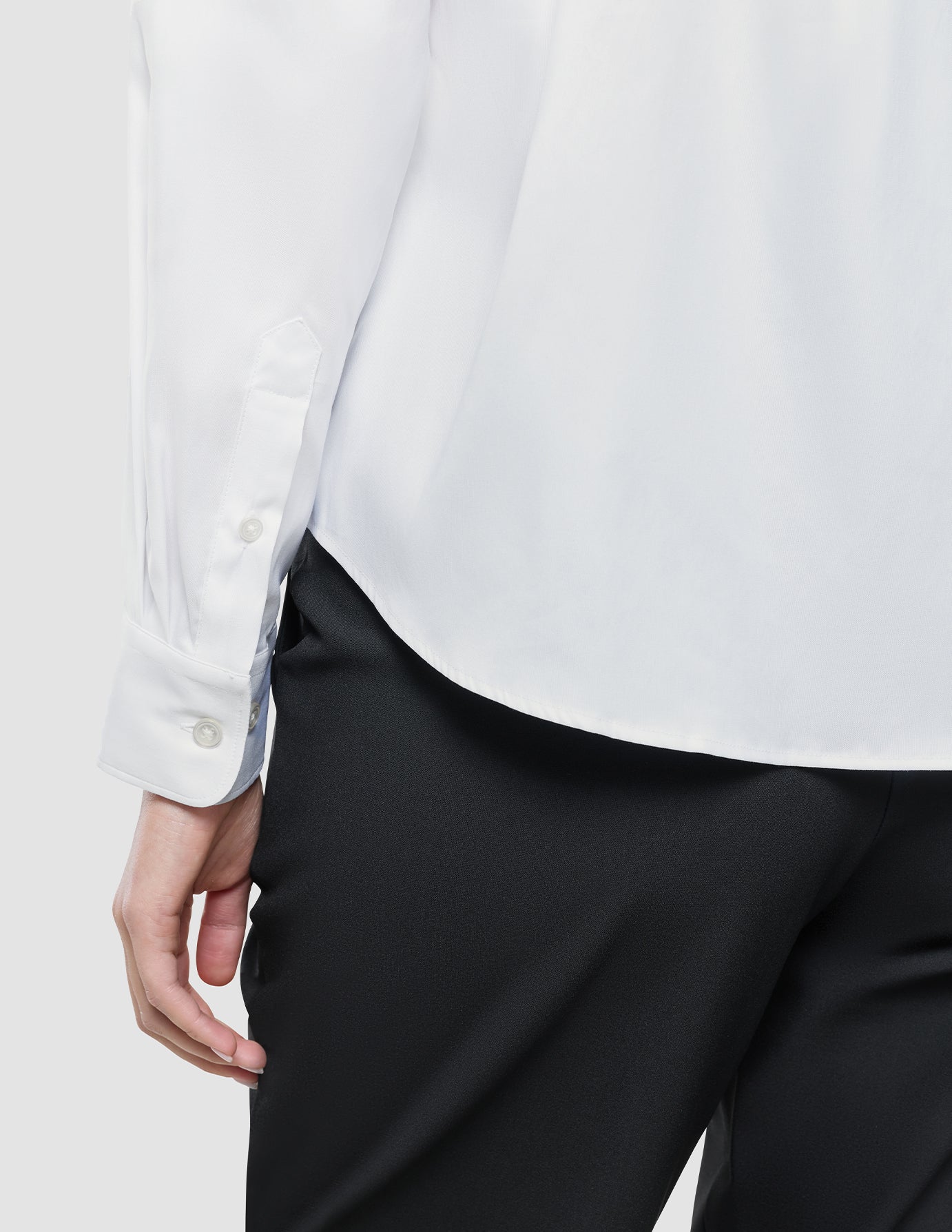 A close-up view of the sleeve and hem of a Women Oxford Shirt White Regular tucked into black trousers.