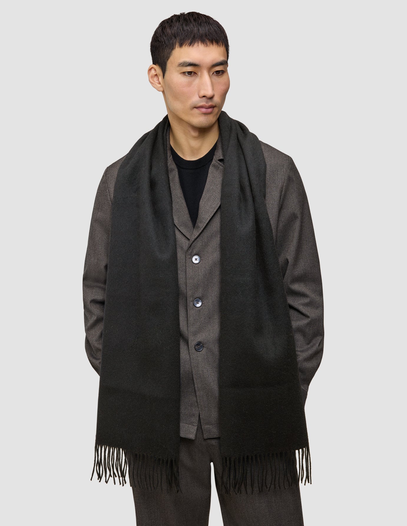 A person wearing a long, fringed Scarf Black over a dark jacket.