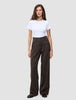 A person wearing a white t-shirt and Serene Pants Wide Walnut Herringbone, which are high-waisted, dark brown pinstriped trousers with a wide-leg silhouette.
