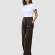A woman stands wearing a white t-shirt and Serene Pants Wide Walnut Herringbone, which are dark, high-waisted wide-leg trousers with thin vertical pinstripes.