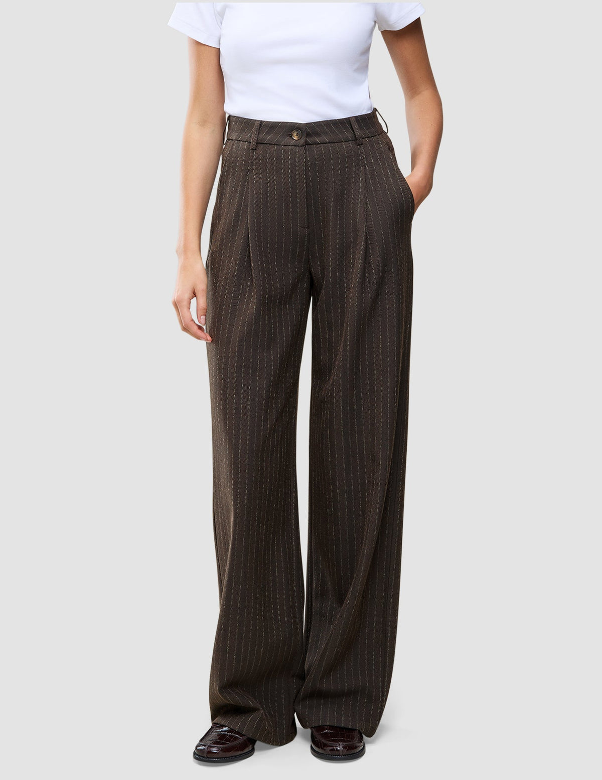 A person wearing Serene Pants Wide Walnut Herringbone in a dark brown pinstripe pattern with a white t-shirt, embodying a minimalist Scandinavian design aesthetic.