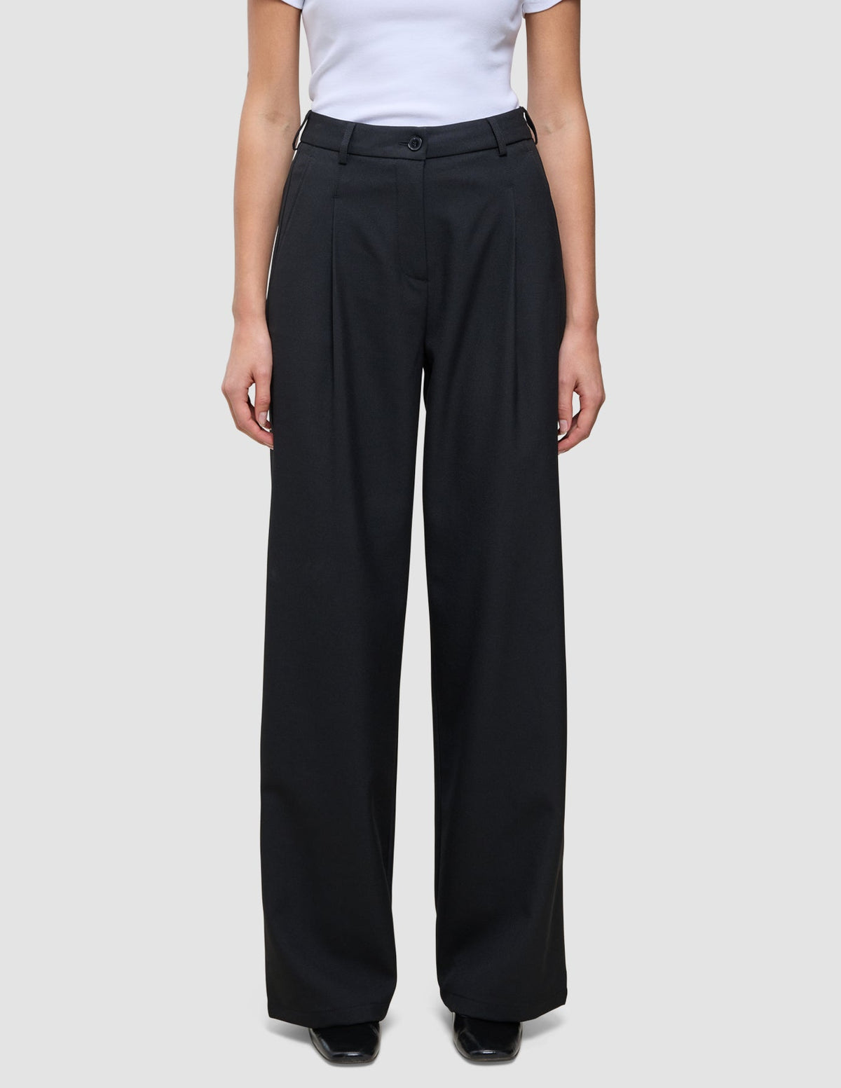 Serene Pants Wide Black featuring high-waisted black wide-leg trousers in a Scandinavian design with front pleats and a button closure.