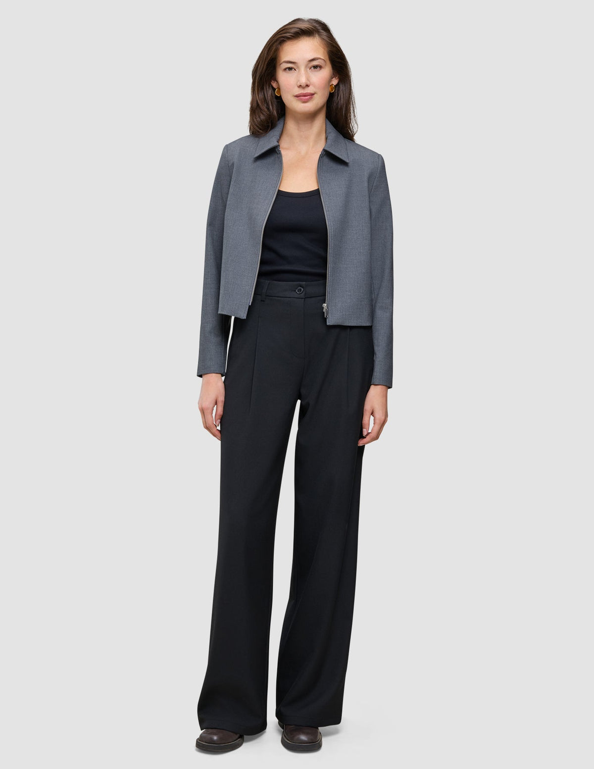 A woman wearing a grey zip-up jacket, a black tank top, and Serene Pants Wide Black.