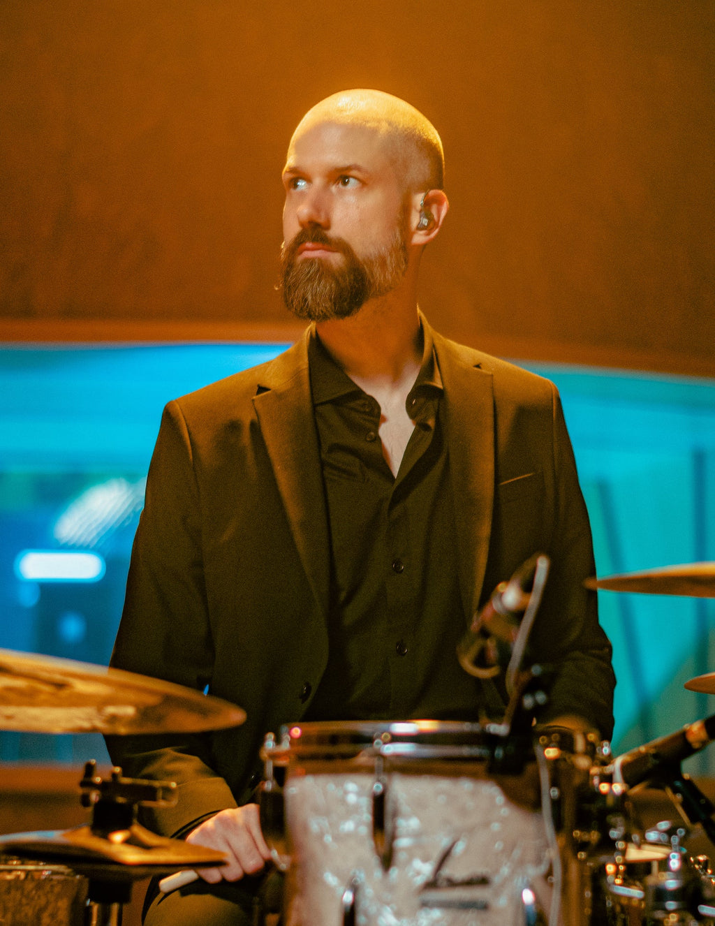 Benny Greb wearing a black suit and black shirt sitting in front of drums