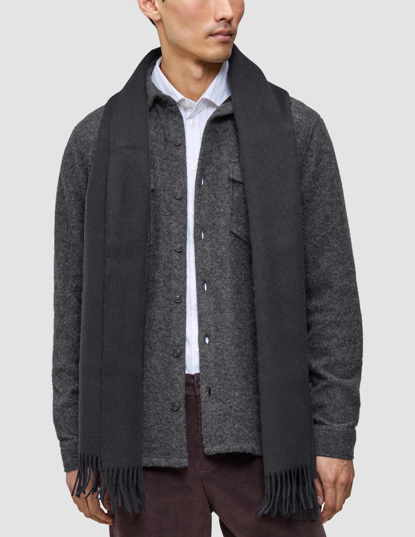 A man wearing a Casual and considered wool button-up shirt over a white collared shirt, accessorized with a long black fringed scarf.