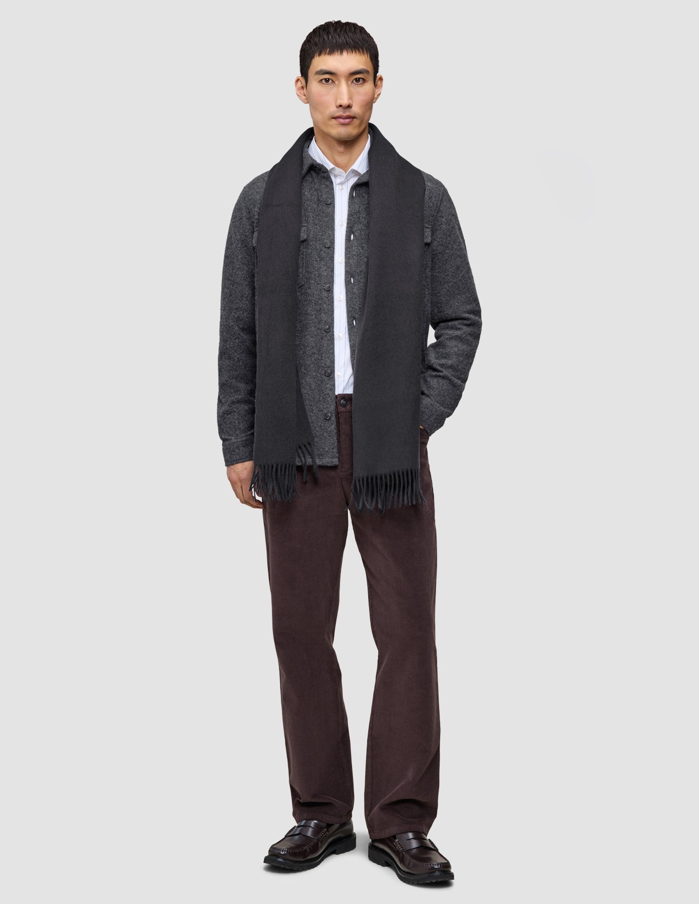 A man in a Casual and considered elevated shirt under a dark grey double layer wool overshirt, long dark grey scarf, brown trousers, and dark loafers.