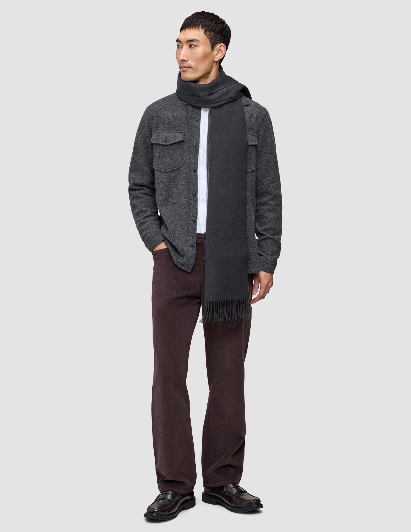 A man wearing a charcoal Casual and considered overshirt over a white undershirt, brown Marco Jeans, and dark loafers.