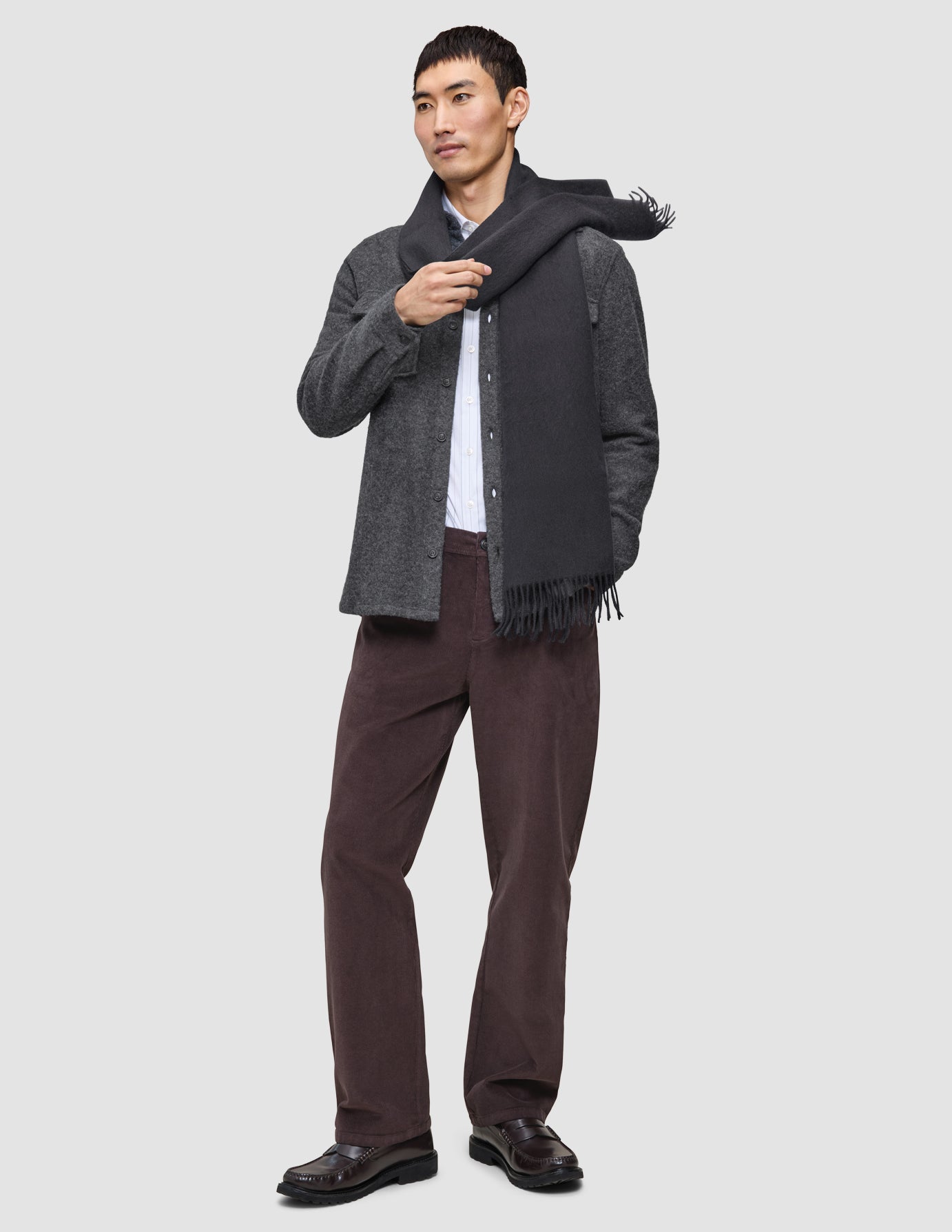 A person dressed in a Casual and considered look, wearing a grey double layer wool overshirt over a white collared shirt, dark Marco jeans, dark shoes, and a grey scarf.