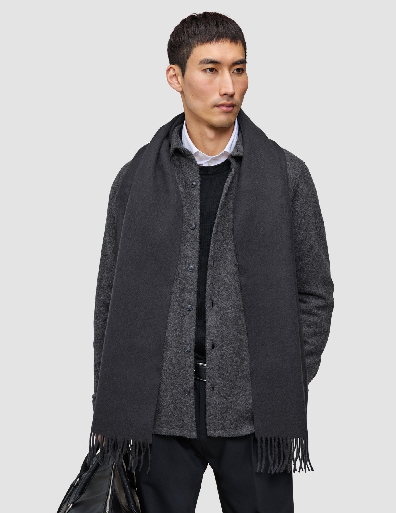 Layers that work: a man wearing a white collared shirt under a premium merino knit sweater, a dark gray double layer wool overshirt, and a long dark gray scarf with fringed ends.