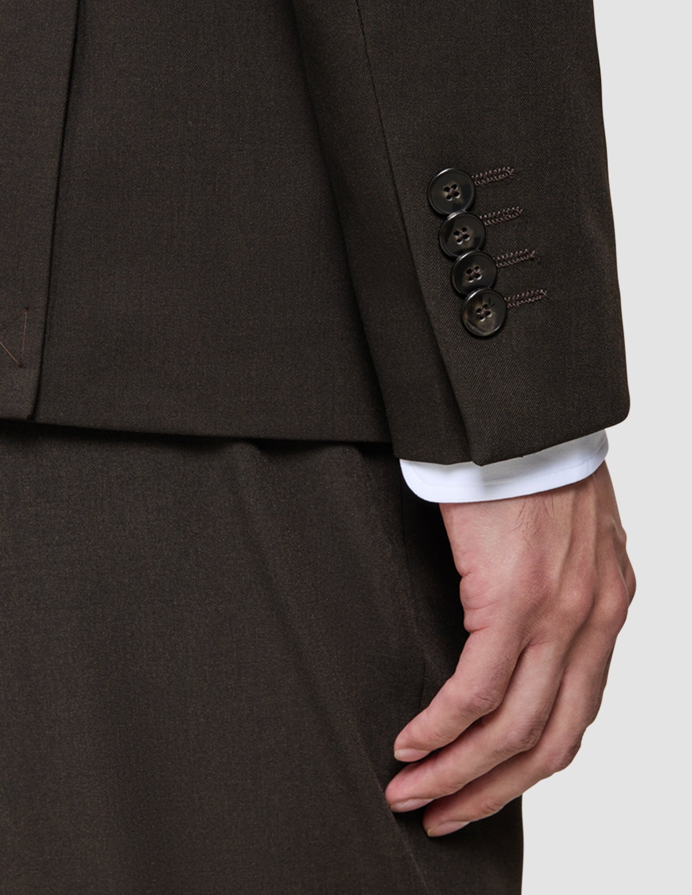 Close-up of a dark brown The suit that does it all jacket sleeve with four buttons, worn over a crisp, elevated white shirt cuff for a classic polished look.