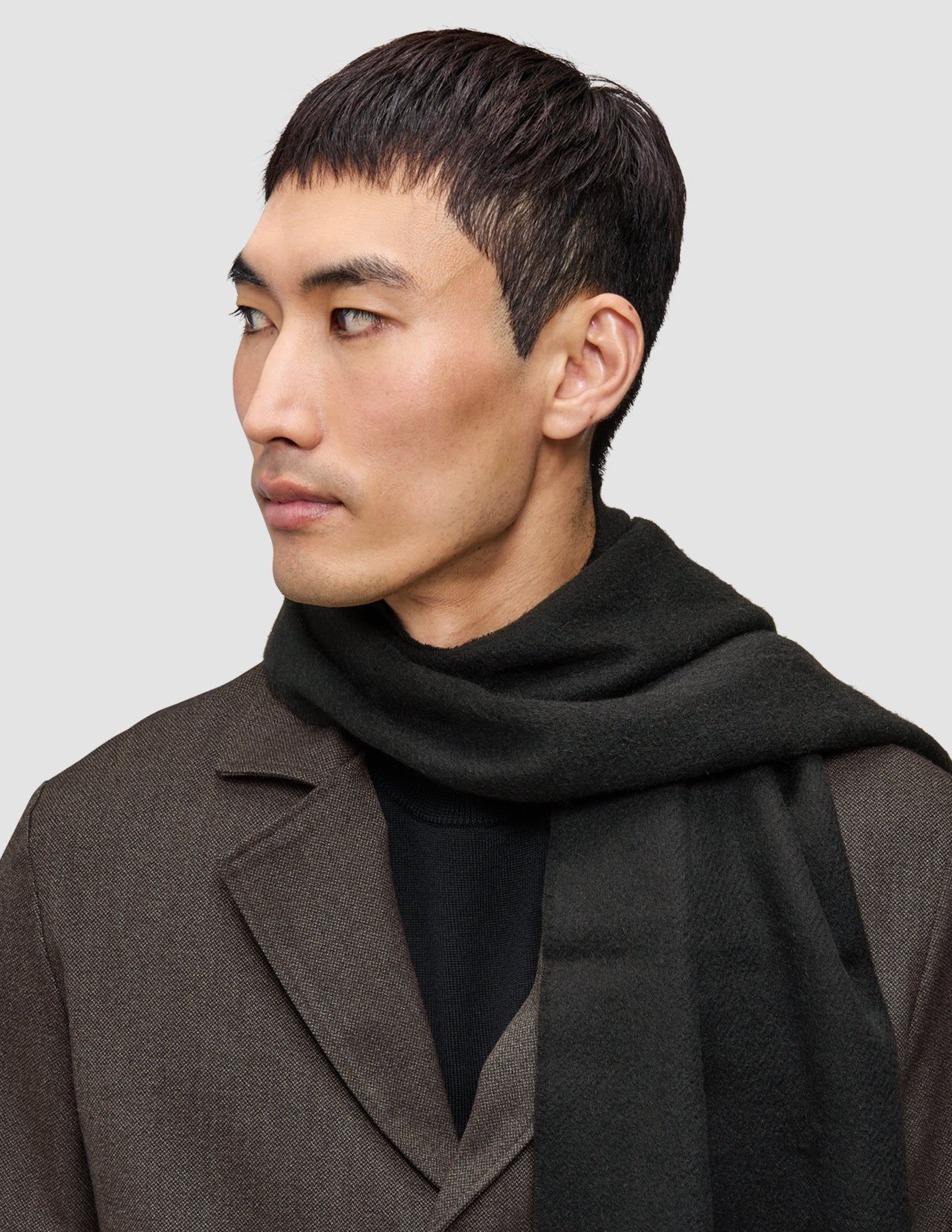 A person wearing an A different kind of suit Atelier Overshirt over a black Merino knit sweater and a dark green scarf.